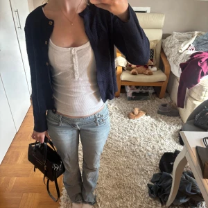 Mörkblå kofta med guldknappar - Snygg mörkblå kofta med guldiga knappar framtill. Modellen är croppad och har långärmade ärmar. Materialet är stickat och koftan har en klassisk, lite loose passform som är enkel att styla till jeans eller kjol. Perfekt för dig som gillar stilrena detaljer.