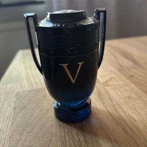 Paco Rabanne Invictus Victory Elixir  - Snygg parfym från Paco Rabanne, modell Invictus Victory Elixir. Flaskan är formad som en pokal i mörkblått glas med svarta detaljer och ett stort gyllene V på framsidan. Perfekt för dig som gillar stilrena och unika designer. Skulle säga att det finns cirka 85 ml kvar :)