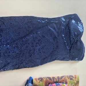 Blå glittrig tubklänning Stylefashion - Snygg blå tubklänning från Stylefashion, täckt med glittriga paljetter som ger en riktigt festlig vibe. Klänningen är kort och axelbandslös, perfekt för dig som vill sticka ut. Materialet är mjukt och följsamt med insida i polyester.