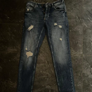 Blå jeans från Gabba, strl 30/32 - Säljer ett par blå jeans från Gabba i modellen Rey K1819 LT. De har slitna detaljer och knappar i gylfen. Jeansen har klassisk femficksdesign och är tillverkade i jeansmaterial. Perfekt för dig som gillar en edgy och modern look.