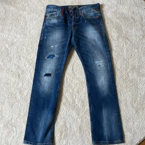 Replay jeans - Säljer ett par blå jeans från Replay i rak modell med slitna detaljer och snyggt tvättad look. Klassiska femficksjeans med kontrastsömmar och broderad logga på bakfickan. Perfekt för dig som gillar streetstyle och vill ha en cool vibe. Priset är ej hugget i Sten 