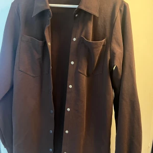 Brun skjorta/ jacka  från Bik Bok XS-S - Snygg brun skjorta från Bik Bok i storlek XS-S. Skjortan har klassisk krage, två bröstfickor och vita knappar framtill. Materialet känns mjukt och är troligtvis bomull. Perfekt att styla med jeans eller kjol för en chill look.