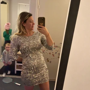 Glittrig silver kortklänning med paljetter - Säljer en glittrig silverfärgad kortklänning med paljetter och mönster över hela klänningen. Klänningen har rund halsringning och trekvartsärm, figurnära passform och är perfekt för att sticka ut. Materialet är syntet med paljettapplikationer.Använd ett par timmar 