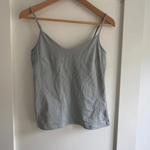 Ljusgrön linnetopp med smala axelband - Snygg ljusgrön linnetopp med smala justerbara axelband och mjuk v-ringning. Toppen är enkel och stilren, perfekt för att matcha med jeans eller shorts. Materialet känns lätt och skönt mot huden, och färgen är neutral vilket gör den lätt att styla.