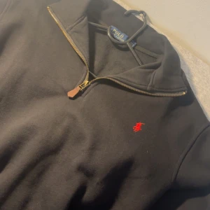 Svart half zip tröja från Polo Ralph Lauren - Skicka dm för video/prisförslag. Svart långärmad tröja från Polo Ralph Lauren med half zip och klassisk röd broderad logga på bröstet. Tröjan har en mjuk bomullskänsla och stilren krage. Perfekt för dig som gillar enkel och snygg design med en touch av lyx.
