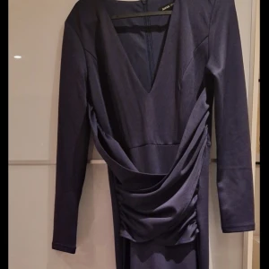 Marinblå långklänning med drapering - Snygg marinblå långklänning med cool drapering över midjan och långa ärmar. Klänningen har en elegant och stilren look, perfekt för dig som gillar att sticka ut med en unik siluett. Materialet känns mjukt och följsamt mot kroppen. Helt ny. 