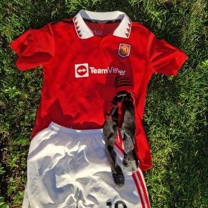 Manchester United Rashford #10 tröja - Säljer en röd Manchester United fotbollströja med Rashford och nummer 10 på ryggen. Tröjan har vit krage med röda detaljer, korta ärmar och TeamViewer-logga på bröstet. Materialet är 100% polyester. Medföljer vita shorts och svarta strumpor med röda ränder och klubbmärke.