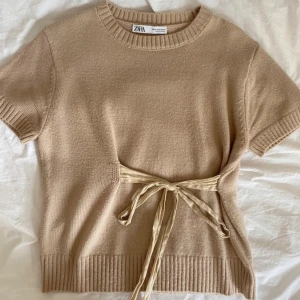 Beige stickad topp med knyt från Zara - Snygg beige stickad topp från Zara med korta ärmar med en roset. Passar även S