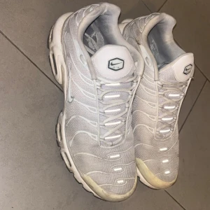Nike Air Max Plus vita sneakers  - Nike Air Max Plus sneakers i helvitt med mesh-överdel och snygga vågiga detaljer. Skorna har synliga Air Max-enheter i sulan, snörning och en platt sula med grå och svarta inslag undertill. Perfekt för dig som gillar sportig och clean stil.