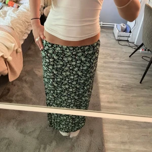 Grön blommig långkjol - Supersnygg långkjol med blommigt mönster i gröna och vita toner. Kjolen har en rak passform och sitter skönt i midjan. Perfekt för dig som gillar en chill och feminin stil. Passar till både sneakers och sandaler.