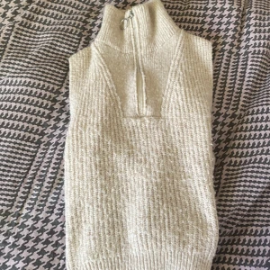 Beige stickad väst från Lindex Kids - Stickad beige väst från Lindex Kids med hög krage och half zip-dragkedja framtill. Västen är ribbstickad och har en mjuk, mysig känsla. Perfekt att slänga över en långärmad tröja för extra värme och stil.❤️