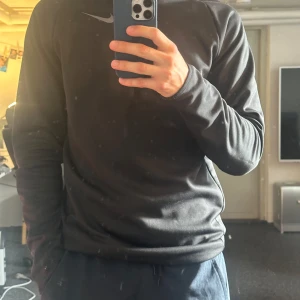Svart långärmad tröja från Nike - En svart långärmad tröja från Nike med dragkedja vid halsen. Tröjan är tillverkad i Dri-Fit material och har en normal passform, storleken är S men passar mer som en medium, jag själv är 185.
