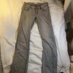 Grå bootcut jeans med knappar - Snygga gråa jeans från Gina Tricot med tre knappar, köpta förra året använda några gånger. Det är ett litet håll på knät men går att fixa enkelt   Storlek 146