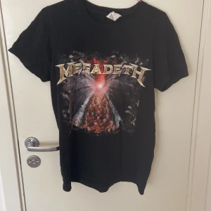 Megadeth Endgame t-shirt svart - Svart Megadeth t-shirt från Gildan med tryck från albumet Endgame. Framsidan har ett stort, färgstarkt motiv och bandets logga, medan baksidan visar låtlistan. Klassisk rund hals och korta ärmar. Mjuk bomull som är skön mot huden.