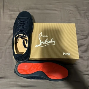 Mörkblå sneakers från Christian Louboutin - Snygga mörkblå sneakers från Christian Louboutin med lyxig mocka och klassisk röd sula med logotyp. Skorna har rund tå, platt sula och snörning. Perfekt för dig som vill sticka ut med exklusiv design och grymma detaljer.