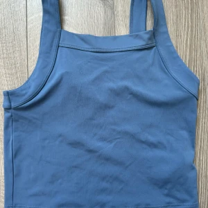 Blå linnetopp från Move, strl 170 - Snygg blå linnetopp från Move med breda axelband och stilren design. Toppen har ett diskret tryck framtill och är gjord i mjukt, stretchigt material som passar perfekt för aktiva dagar. Enkel och sportig look som är lätt att matcha med dina favoritplagg.