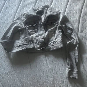 Grå  jeansjacka från ONLY - Säljer en grå jeansjacka från ONLY med coola detaljer som dubbla bröstfickor med knappar och markerade sömmar. Jackan har klassisk krage, långa ärmar och knäppning framtill. Perfekt för dig som gillar en edgy och trendig look.