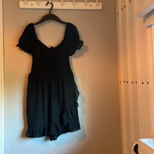 Svart kort klänning newyorker XXS - Supersöt svart kort klänning från newyorker i storlek XXS,aldrig andvänd. Klänningen har puffiga korta ärmar, smockad överdel och volangdetaljer längst ner. Materialet är lätt och har diskreta prickar, samt en knytning framtill för extra stilpoäng.