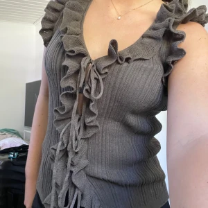 Grön ribbad volangtopp från Zara - Supersnygg mörkgrön/oliv/ gråaktig ribbad topp från Zara med volanger. Djup v-ringning och knyt framtill ger en unik look. Ärmlös modell som sitter figurnära och känns både trendig och cool. Endast provad 