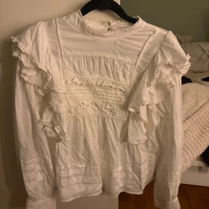 Vit volangblus från BikBok - Supersöt vit blus från BikBok med volanger och dekorativa sömmar framtill och på ärmarna. Blusen har lång ärm, hög halsringning och knäppning bak i nacken. Det är i storlek M men passar ifall du har S då jag har det själv.❤️säljer denna då den inte kommer alls till användning