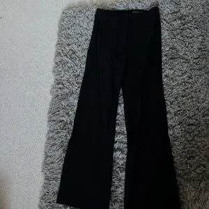 Svarta kostymbyxor från Stockh LM - Snygga svarta kostymbyxor från Stockh LM med klassisk rak passform och vida ben. Byxorna har hög midja och stilrena detaljer, perfekta för en clean och trendig look. Superskönt och Stretchigt jerseymaterial samtidigt som de ser formella ut!