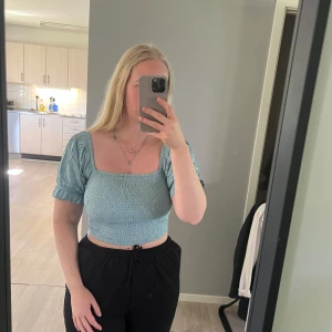 Ljusblå croppad topp med puffärm - Säljer en ljusblå croppad topp med smockad midja och puffiga korta ärmar. Toppen har fyrkantig ringning och kan bäras både med axlarna uppe eller offshoulder. Storlek s, från bikbok 