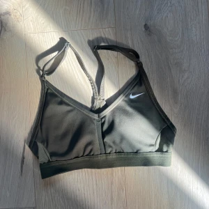 Olivgrön sporttopp från Nike Xs - Olivgrön sporttopp från Nike med justerbara tunna axelband och vit logga framtill. Snygg och enkel design med bred resår under bysten för extra stöd. Perfekt för all form av träning. Säljer pga den inte passar mig  💗