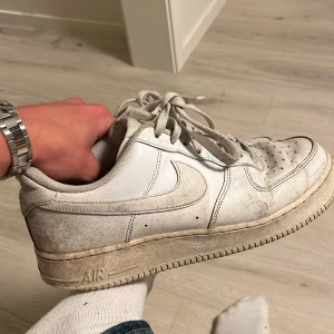 Nike Air Force 1 vita sneakers - Klassiska Nike Air Force 1 sneakers i helvitt skinn med rund tå och snörning. Snygg och tidlös modell med perforerade detaljer på tån och robust sula. Perfekta för dig som gillar streetstyle och vill ha en ikonisk sneaker i garderoben.