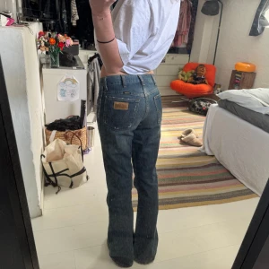 Wrangler blå bootcut jeans - Säljer ett par klassiska blå jeans från Wrangler med bootcut passform. Storlek 28/32. Jeansen har hög midja, raka ben som blir vidare nertill och snygga detaljer på bakfickorna. Tillverkade i slitstarkt denim med en mörkblå tvätt och läderpatch bak.
