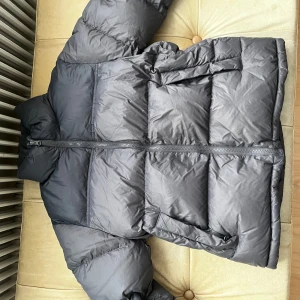 Svart pufferjacka från Singular society - Säljer en svart pufferjacka från Singular society med hög krage och dragkedja framtill. Jackan är vadderad och har två stora fickor på sidorna. Perfekt för kalla dagar och har en clean, stilren look som funkar till det mesta.