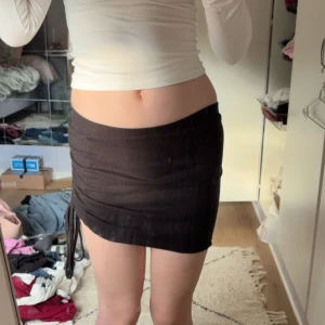Svart ribbad minikjol med snörning - Svart kortkjol i ribbat material med snörning på sidan som ger en snygg rynkad effekt. Kjolen sitter tight och har en enkel, stilren look som passar perfekt till crop tops eller oversized tröjor.