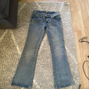  7 For All Mankind - Säljer ett par blå flare jeans från 7 For All Mankind med snygga detaljerade bakfickor. Jeansen är tillverkade i 98% bomull och 2% lycra för en skön stretch. Klassisk femficksmodell och tillverkade i USA. Perfekta för dig som gillar retrovibbar och cool passform.