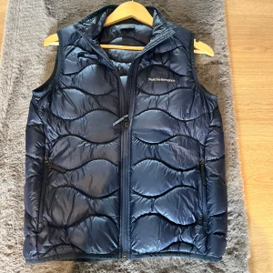 Mörkblå dunväst från Peak Performance - Snygg mörkblå dunväst från Peak Performance med vågformat quiltat mönster. Nästan aldrig använd! Skriv för frågor!