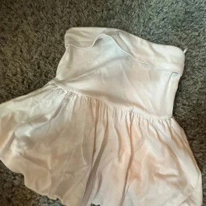 Vit axelbandslös topp Gina Tricot - Supersöt vit axelbandslös topp från Gina Tricot. Klänningen har en volangig kjol och sitter snyggt över bysten. 