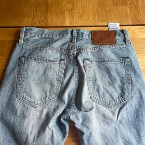 Levi's 501 ljusblå jeans W28 L32 - Ljusblå Levi's 501 jeans med klassisk rak passform och fem fickor. Jeansen har knappgylf, bruna sömmar och det ikoniska läderpatchen bak i midjan. Tror dessa är manmodell men jag har använt dessa ändå och tycker de sitter jättesnyggt - men med detta sagt är de tajtare i midjan och runt låren än en kvinnlig storlek 28:)