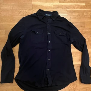Mörkblå overshirt Ralph Lauren - Säljer en mörkblå overshirt/skjorta från Polo Ralph Lauren. Storlek är M och passar om man är 175-185 cm lång. Knappen vid fickan har gått sönder lite men inget som påverkar eller syns mycket