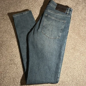 jeans från J.Lindeberg - Snygga blå jeans från J.Lindeberg med klassisk femficksdesign och smal passform. Jeansen har en mörk tvätt och raka sömmar, tillverkade i mjukt denimtyg. Perfekta för en stilren och modern look. Ny pris 2000kr mitt pris 350kr