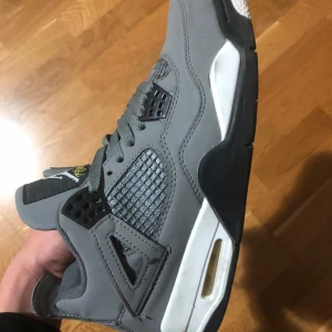 Nike Air Jordan 4 Retro Cool Grey - Snygga Nike Air Jordan 4 Retro i färgen Cool Grey. Skorna har grå mocka med svarta och vita detaljer, samt gula accenter på sulan och tungan. Klassisk siluett med snörning och meshpaneler på sidorna. Perfekta för dig som gillar streetwear och ikoniska sneakers. Jorden 4 Retro cool grey i bra skick, kommer utan orginiala boxen.