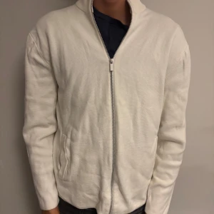 Vit kofta med dragkedja - Snygg vit kofta med hel dragkedja framtill och två fickor på sidorna. Tröjan har en enkel och clean look med långärmad passform och ribbad krage. Perfekt för lager-på-lager och passar till det mesta i garderoben.