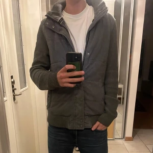 Cardigan med stickad armar från S.Oliver - skriv gärna om funderingar eller prisförslag! Säljer en stilren grå cardigan jacka  med dragkedja och knappar. Jackan har långa ärmar och ribbade muddar. Perfekt för våren och sommaren.