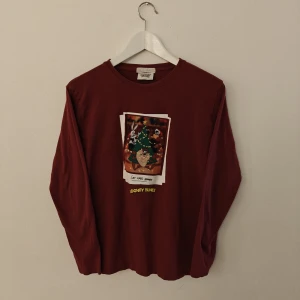 Looney Tunes tröja - Säljer en vinröd långärmad tröja från Looney Tunes med ett juligt tryck framtill. Tröjan är i 100% bomull och har en klassisk rund halsringning. Perfekt för dig som gillar tecknade motiv och vill ha något bekvämt och snyggt.