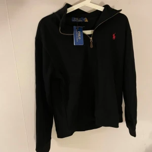 Svart half zip tröja från Polo Ralph Lauren - Svart långärmad tröja från Polo Ralph Lauren med half zip och klassisk röd logga broderad på bröstet. Tröjan är i bomull och har en stilren look som passar perfekt till jeans eller chinos. Snygg och enkel att matcha med det mesta. Den passar XS, helt ny.