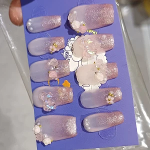 Rosa glittriga lösnaglar med dekorationer - Säljer ett set med rosa lösnaglar med glitter och 3D-dekorationer som pärlor, blommor och rosetter. Naglarna har en mjuk ombre-effekt från ljusrosa till glittrigt rosa och är dekorerade med små guldpärlor och plastrosor för en extra söt look.