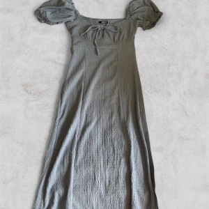 Grå/blå långklänning från Gina Tricot - Supersnygg grå långklänning från Gina Tricot med puffiga kortärmar och en söt knytning framtill. Klänningen har en lätt skrynklig struktur och sitter bekvämt med normal passform. Perfekt för dig som gillar ikoniska och trendiga plagg. Pris kan diskuteras vid snabb affär❤️