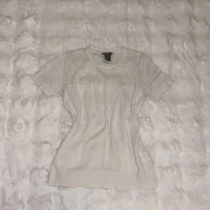 Vit stickad topp från Lindex - Snygg vit stickad topp från Lindex med korta ärmar och rund hals. Överdelen och ärmarna har ett coolt stickat nätmönster som ger en modern vibe. Perfekt till jeans eller kjol för en clean och fräsch look.