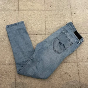 Ljusblå Replay jeans  - Säljer ett par ljusblå jeans från Replay med klassisk femficksdesign och snygga detaljer på fickorna. Jeansen  är tillverkade i stretchigt denim för en bekväm känsla. Perfekta till sneakers och hoodie. En liten defekt vid bakfickan på jeansen. Inte så stor men ett litet hål.. Därav priset!