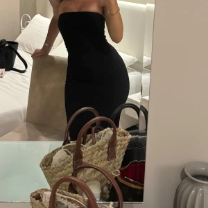 Svart axelbandslös långklänning - Säljer en svart, figurnära långklänning med axelbandslös design. Klänningen har en clean och stilren look som framhäver siluetten. Perfekt för dig som gillar minimalistisk stil och vill ha en klänning som sitter snyggt och bekvämt. Kostym material