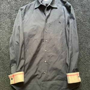 Svart Burberry skjorta med rutig detalj - Mörkblå Burberry skjorta.                                    Storlek S/M.                                                    Skick 7/10.                                               Kom privat vid frågor å funderingar😊