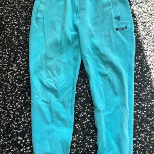 Turkosa mjukisbyxor från BOSS - Snygga turkosa mjukisbyxor från BOSS med logga på ena fickan. Byxorna har en relaxed passform och är perfekta för chill dagar. Mjukt material och elastisk midja för extra komfort.
