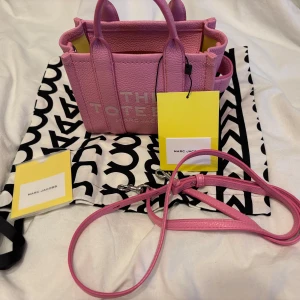 Rosa The Tote Bag från Marc Jacobs - Superfin rosa The Tote Bag från Marc Jacobs i skinn med gul insida. Väskan har både handtag och avtagbar axelrem, perfekt för att bära på olika sätt. Kommer med dustbag och originaltaggar. Snygg och trendig modell med tydlig logga framtill.